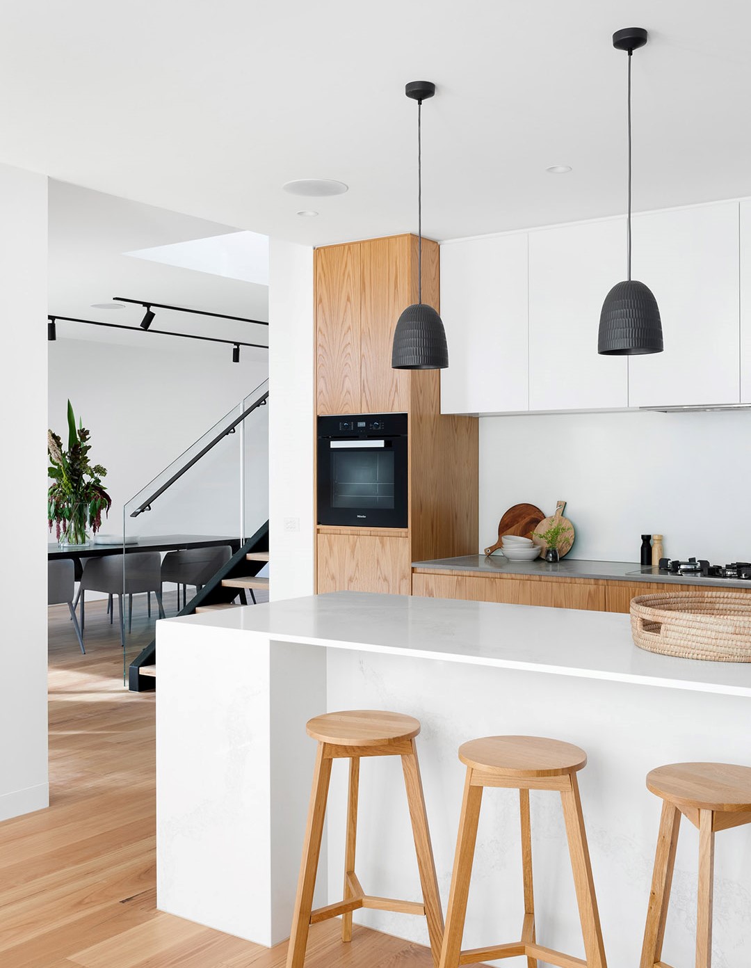 View of a white kitchen with an island and barstools, looking left to another room