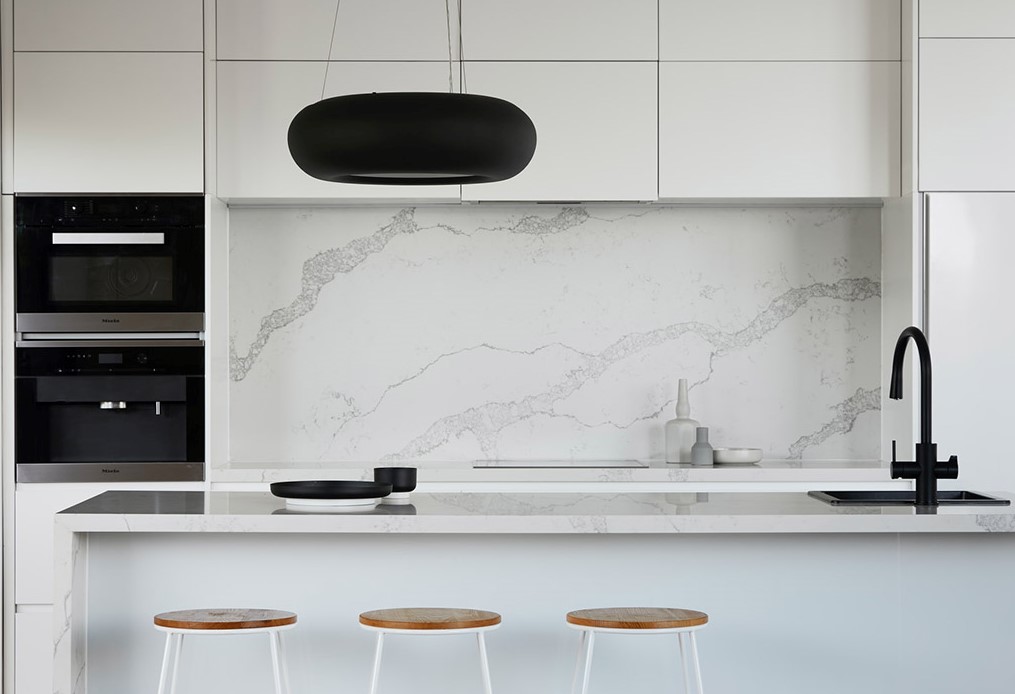 White marble kitchen with double ovens, sinks and island with bar stools.