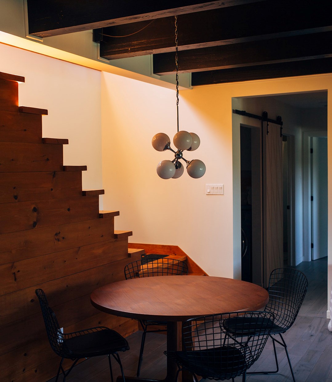 Low hanging light fixture over a table with stairs up in the background.